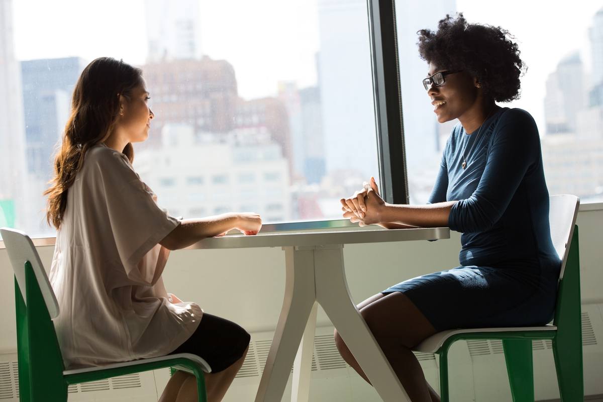 Two professionals in conversation at a table by a large window